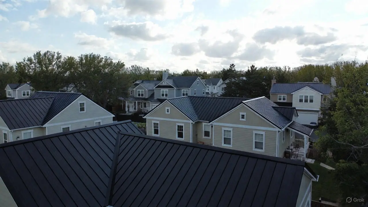 An aerial view of a residential neighborhood featuring multiple homes with a sleek black standing seam metal roof, showcasing the uniform vertical ribs and modern aesthetic under a cloudy sky